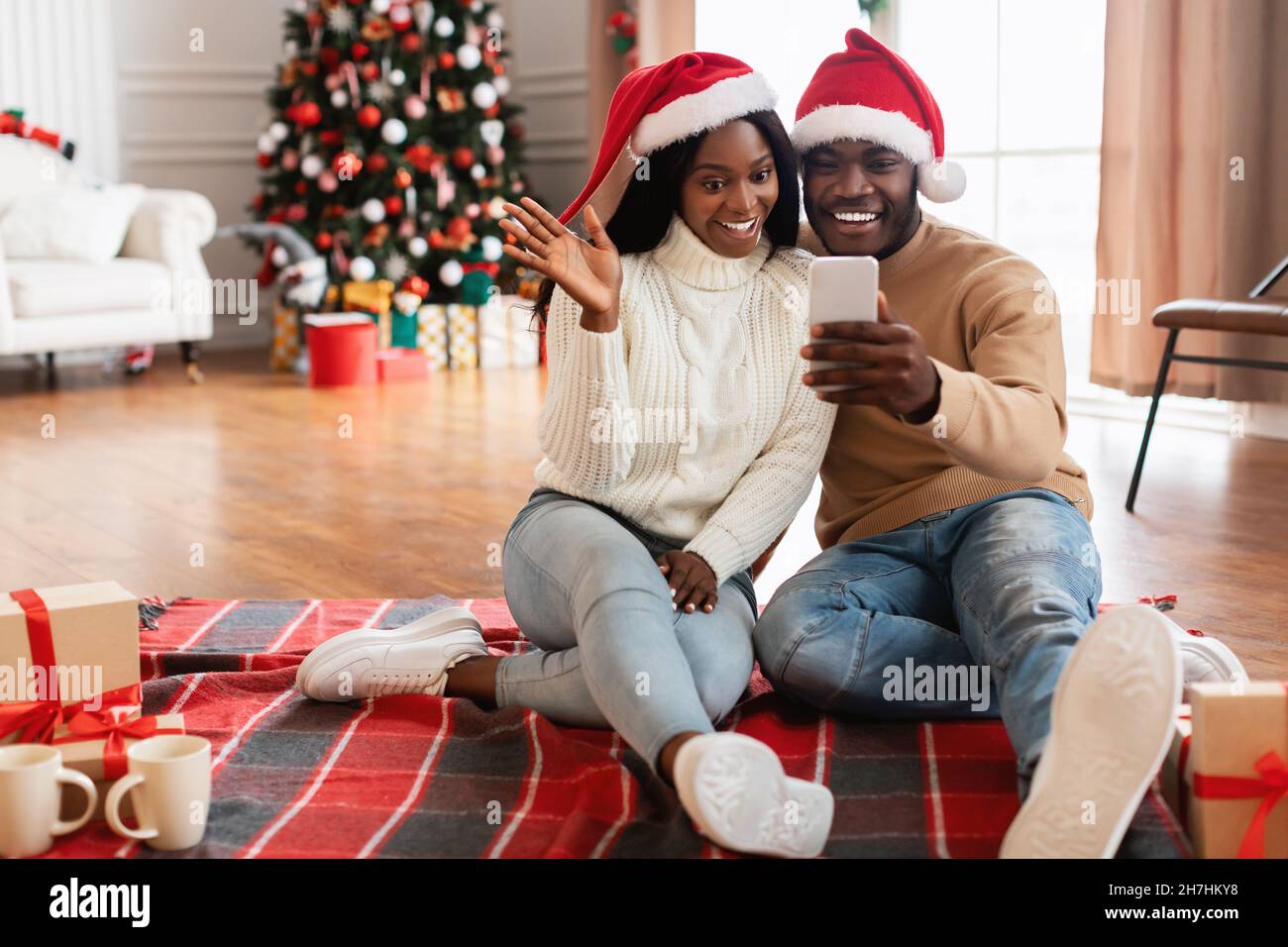 Famiglia nera che usa il cellulare che fa la videocall su mani sventolanti di Natale Foto Stock