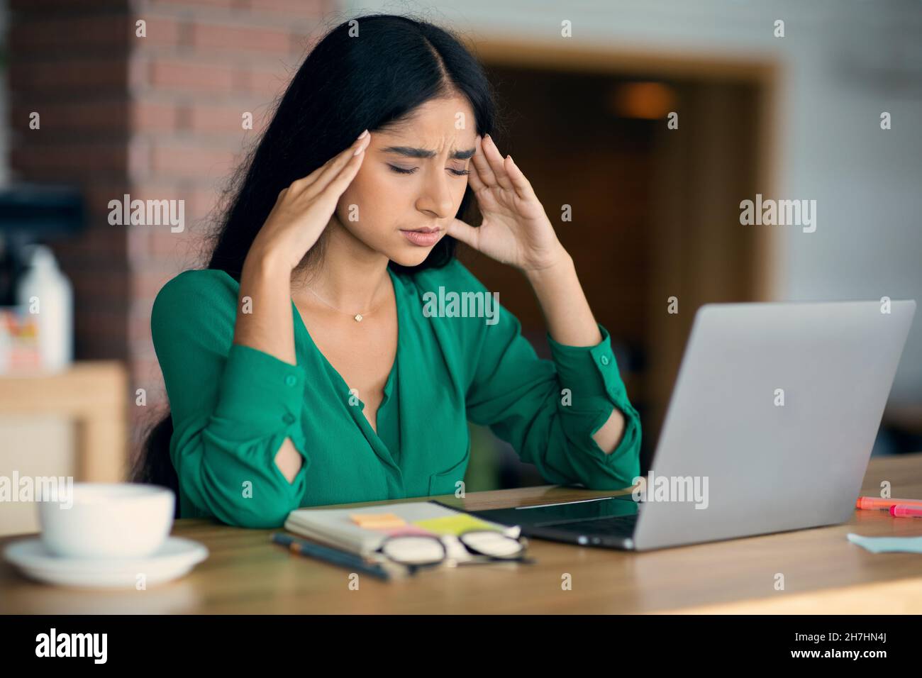Stressata giovane donna arabica usando il laptop al caffè Foto Stock