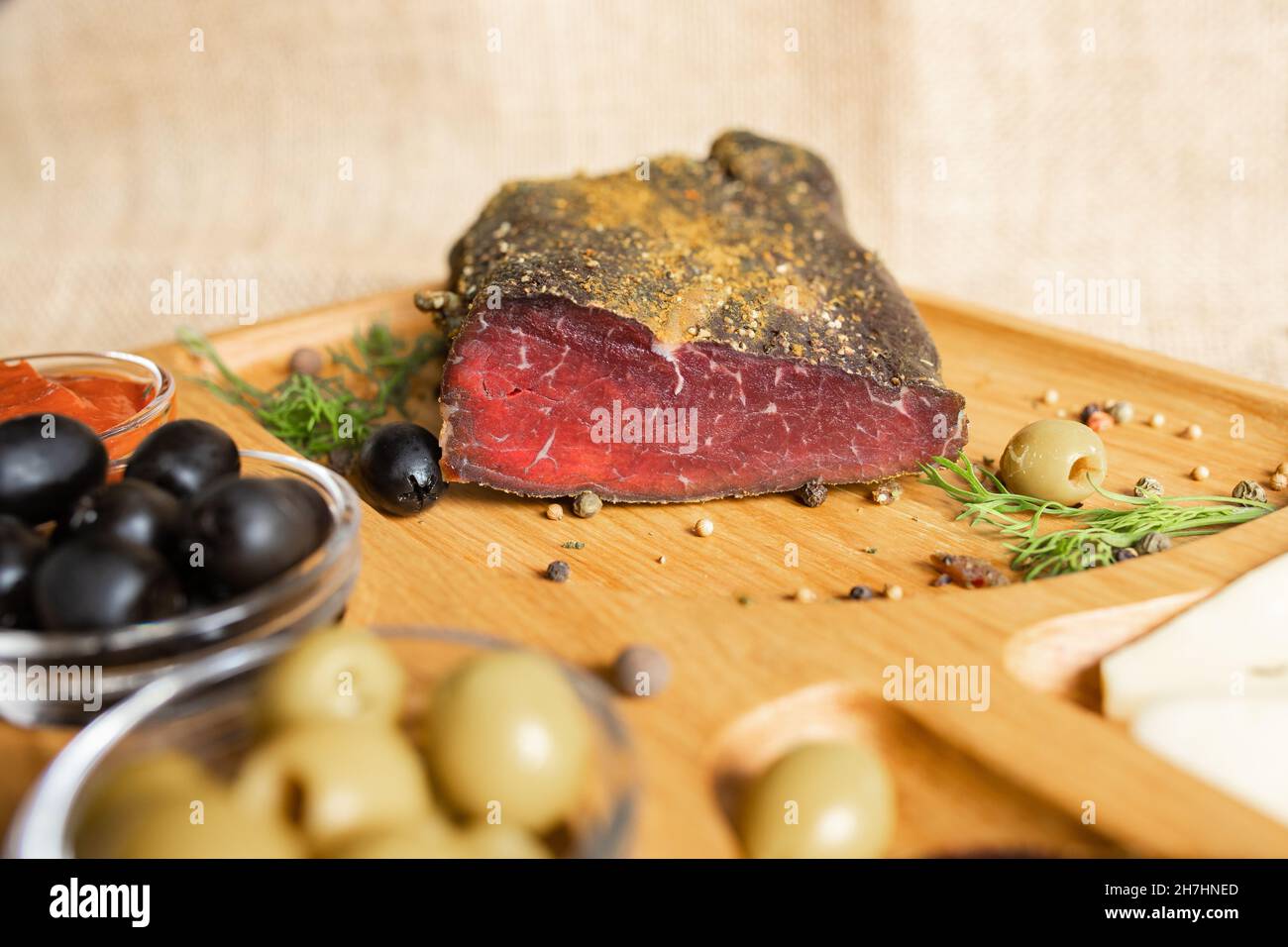Filetto secco di carne di manzo, tagliato a fette sottili, sul piatto di legno con formaggio, olive, pepe nero, salsa di pomodoro. Antipasto con filetto a scatto Foto Stock
