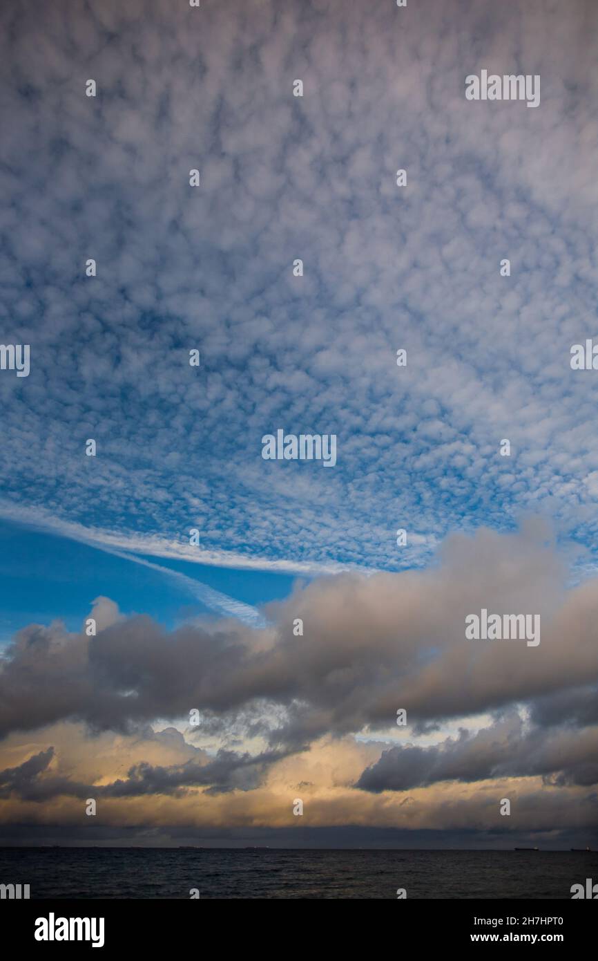 Cielo mozzafiato sul mare con sole che illumina le nuvole bellissimo cielo blu sopra il mare con diverse nuvole bianche, grigie e gialle illuminate dal sole Foto Stock