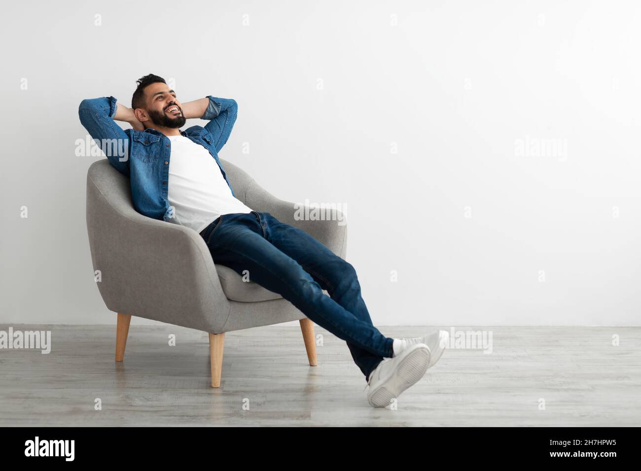 Calma giovane uomo arabo rilassarsi in poltrona contro il muro bianco studio, spazio copia Foto Stock