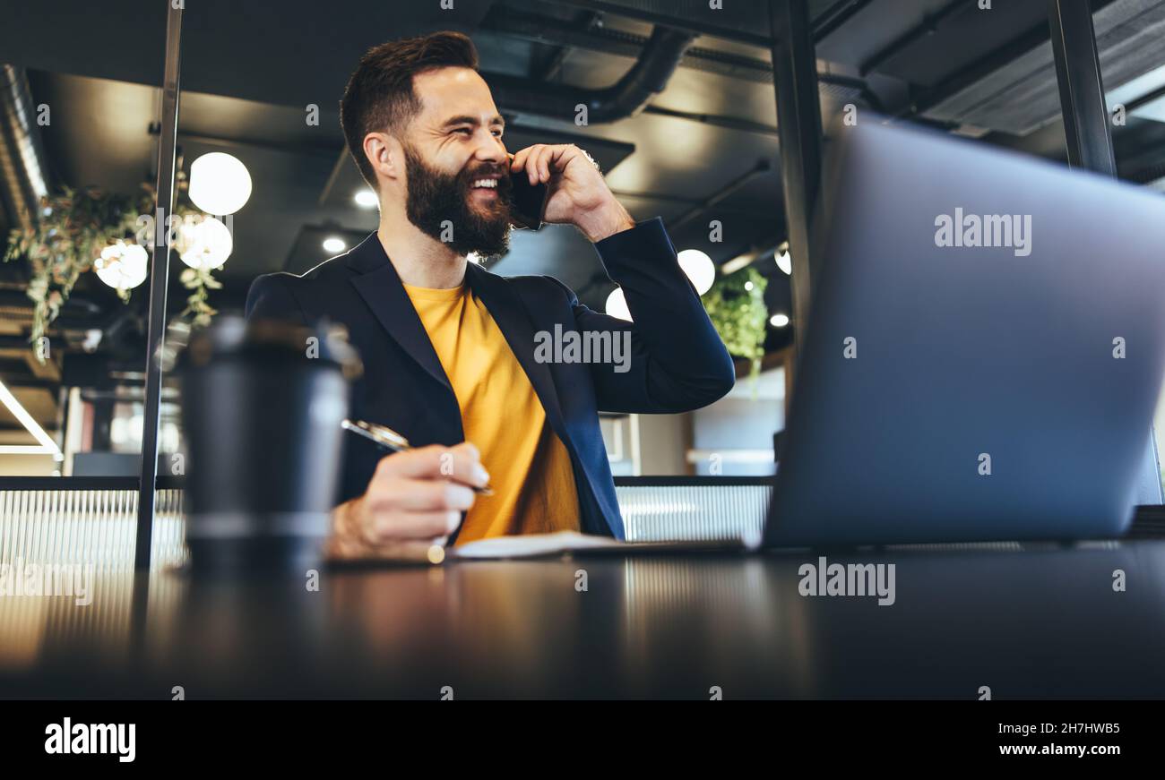 Un uomo d'affari felice sorridendo durante una telefonata. Giovane uomo d'affari che scrive le note mentre comunica con i suoi clienti in un ufficio. Imprenditore allegro Foto Stock