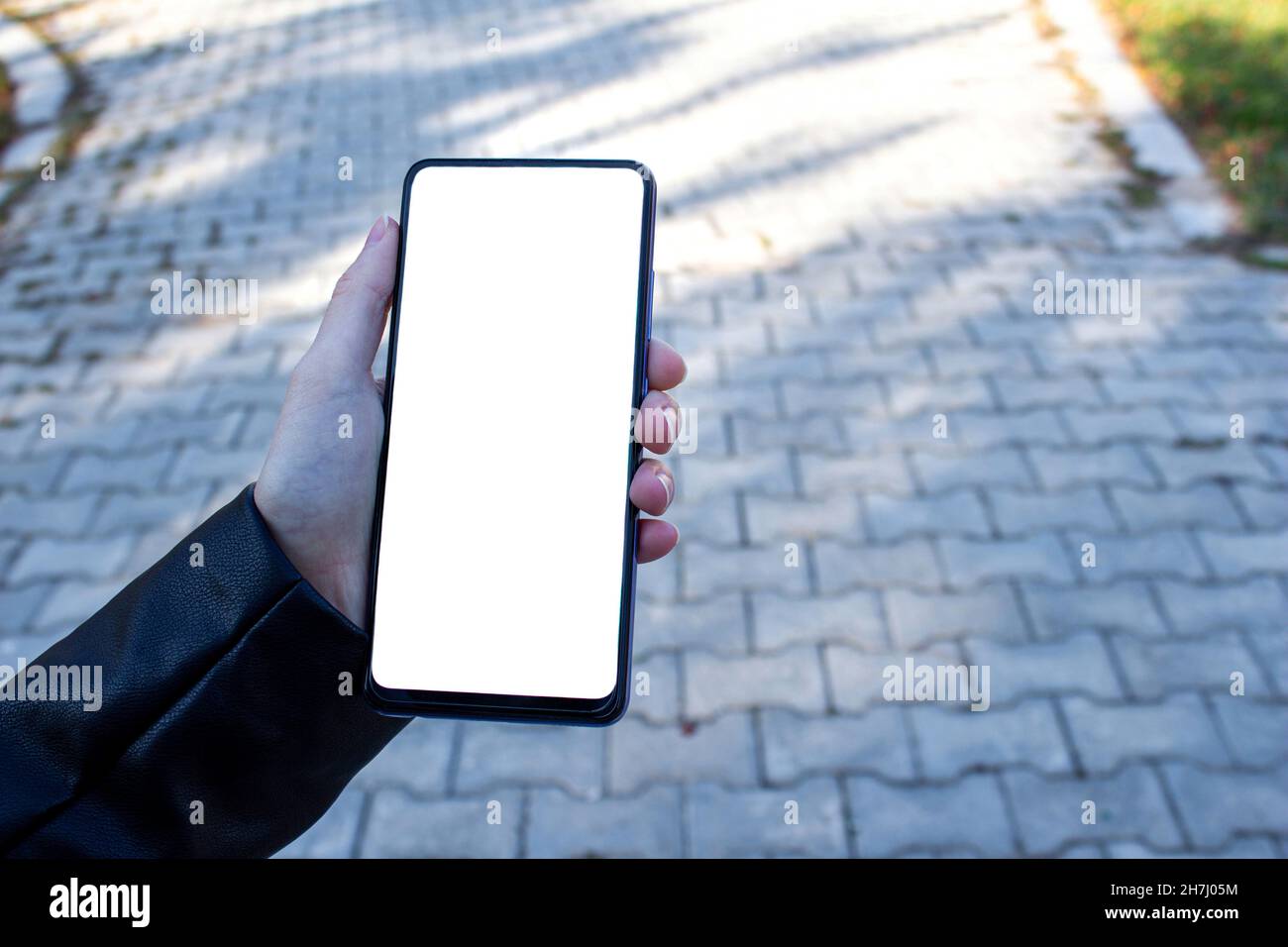 Immagine mockup di una mano donna che tiene il telefono cellulare con schermo bianco vuoto mentre si cammina sul marciapiede. Foto Stock