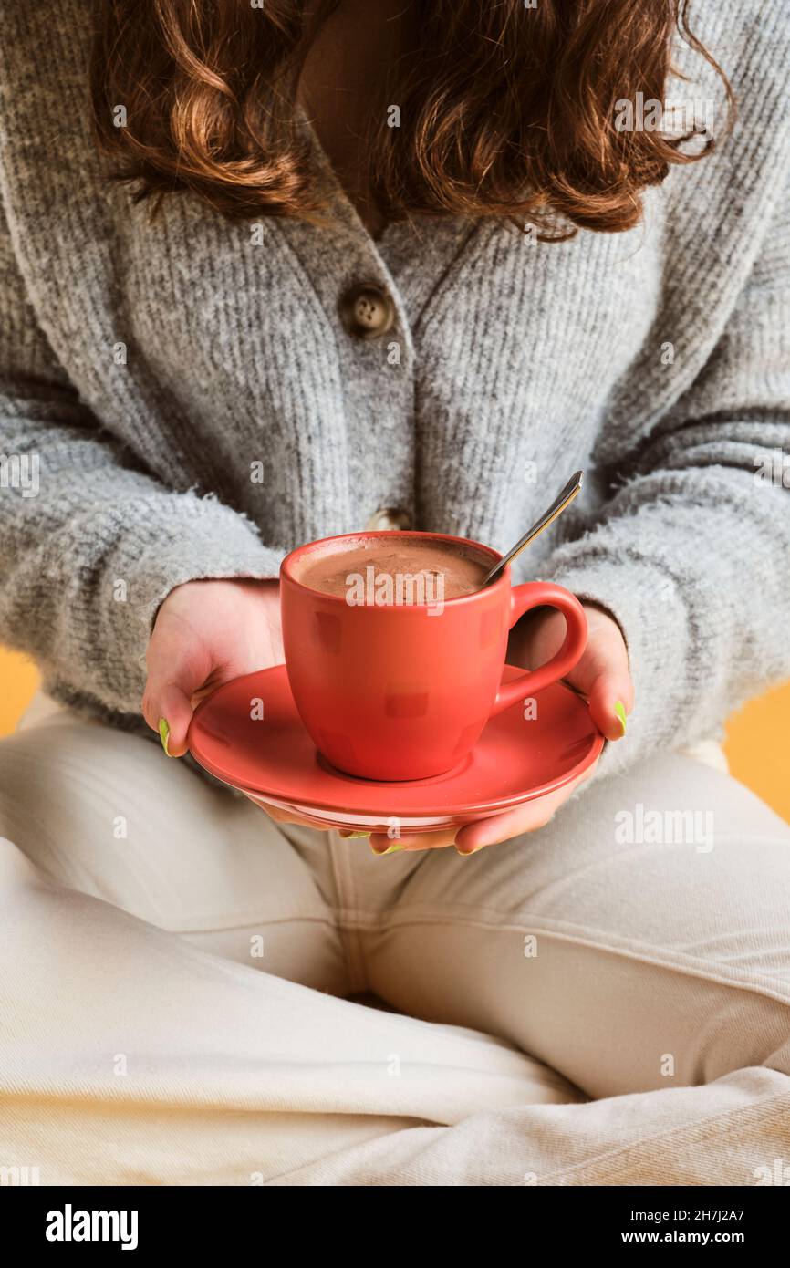 Ragazza accogliente seduta sul pavimento con una tazza rossa con cioccolata calda e latte Foto Stock