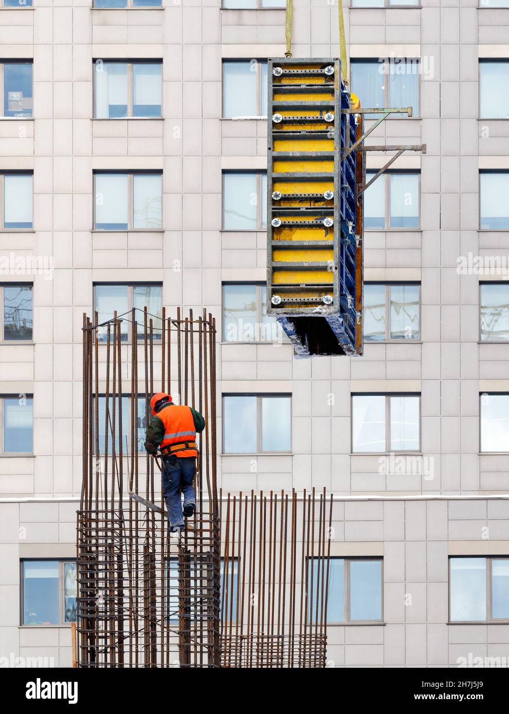 Un costruttore che indossa un gilet arancione brillante e un casco di sicurezza installa la cassaforma su un telaio in acciaio per la successiva colata di calcestruzzo. Foto Stock