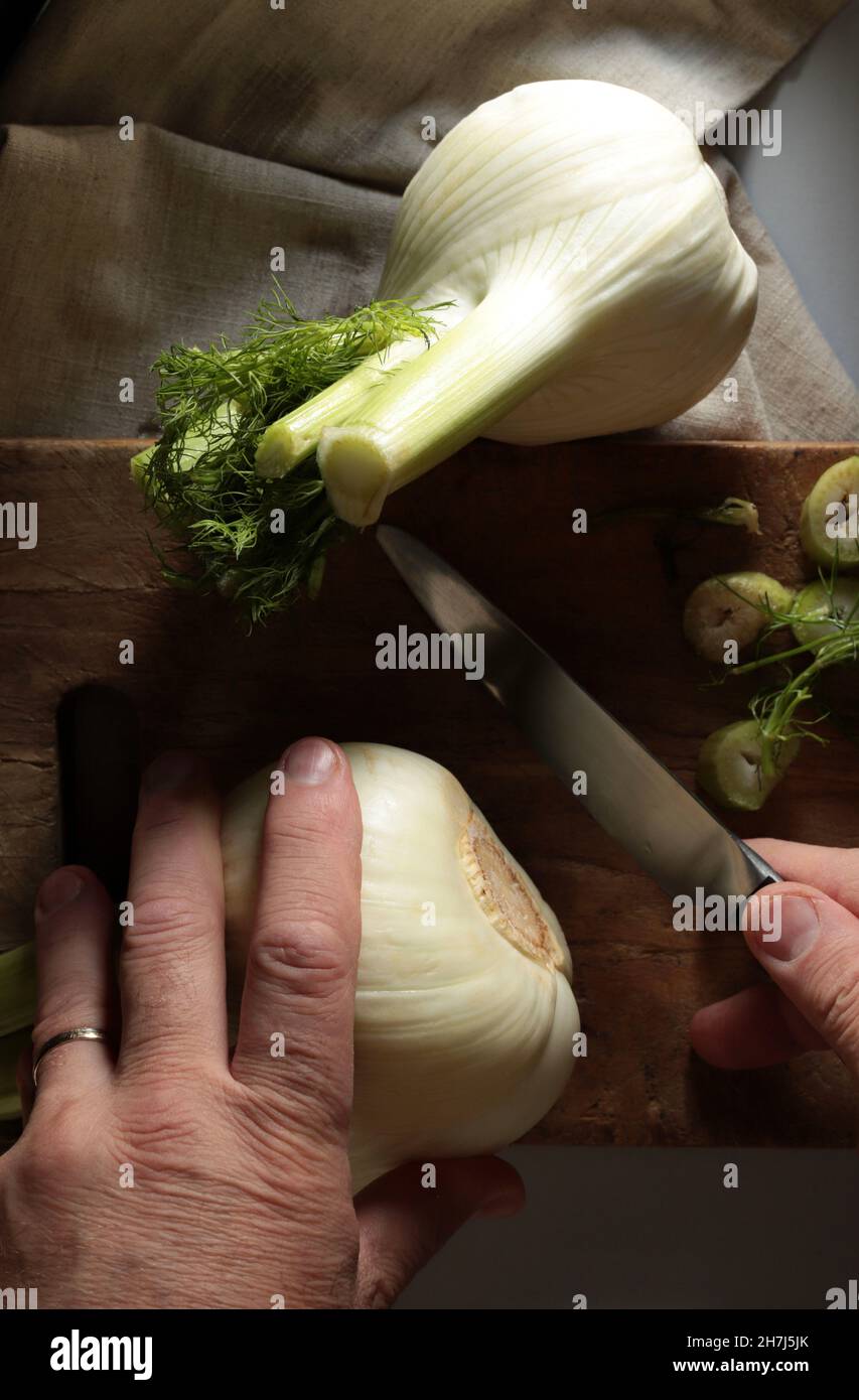 Primo piano di un finocchio per affettare un uomo su un tagliere di legno. Sfondo scuro. Direttamente sopra. Foto Stock