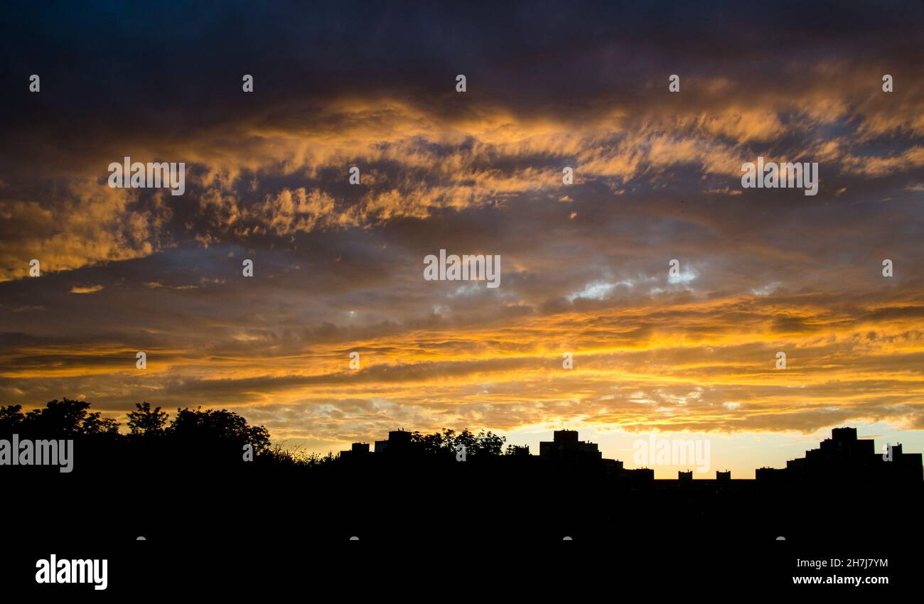 Cielo tempestoso nel fuoco del tramonto e paesaggio urbano dal profilo nero. Nuvole brucianti di tempesta imminente Foto Stock