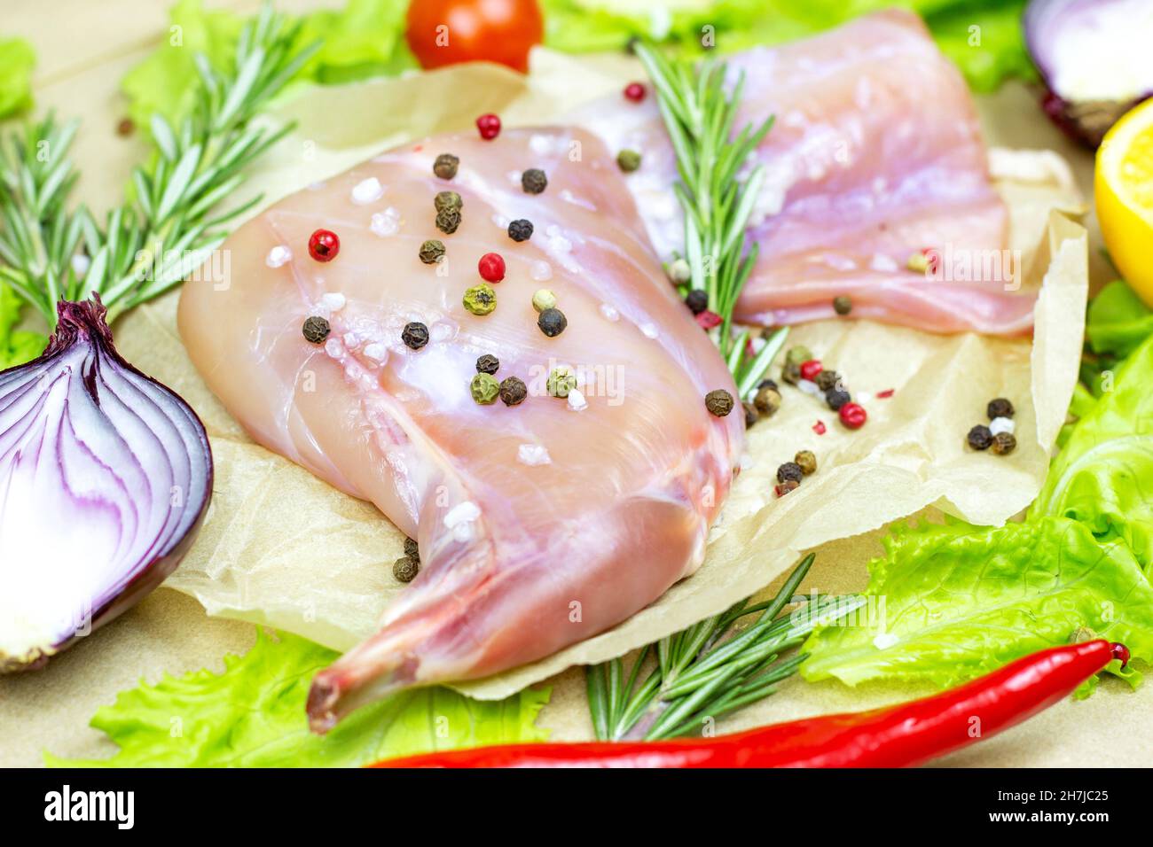 Carne cruda di coniglio rosa non cotta con rosmarino verde e verdure fresche su fondo di tagliere di legno chiaro. Foto Stock