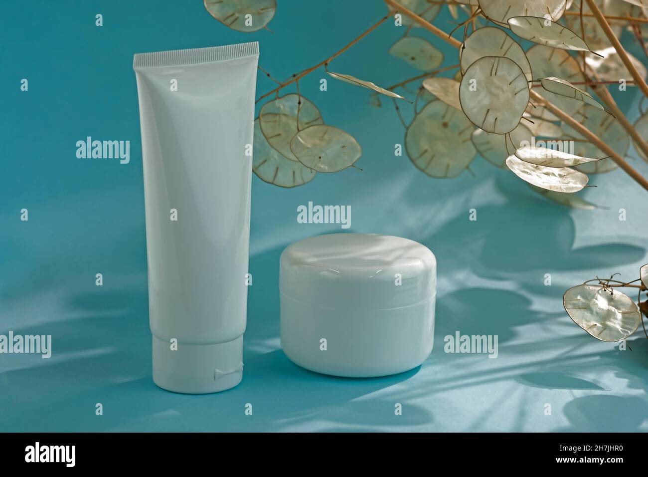 Contenitori in plastica bianca per crema su sfondo blu. Concetto di cosmetici naturali. Svuotare la provetta bianca e il recipiente per la crema. Foto Stock