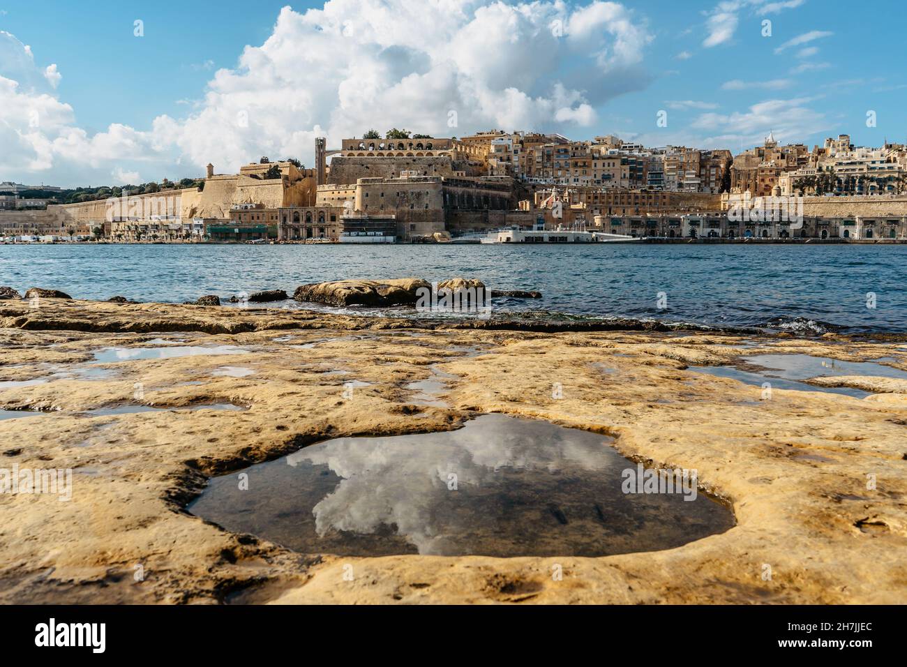 Vista panoramica della Valletta, Malta. Skyline della città dal porto di Birgu Vittoriosa. Paesaggio urbano tranquillo, giorno d'estate soleggiato, nuvole riflesse nell'acqua Foto Stock