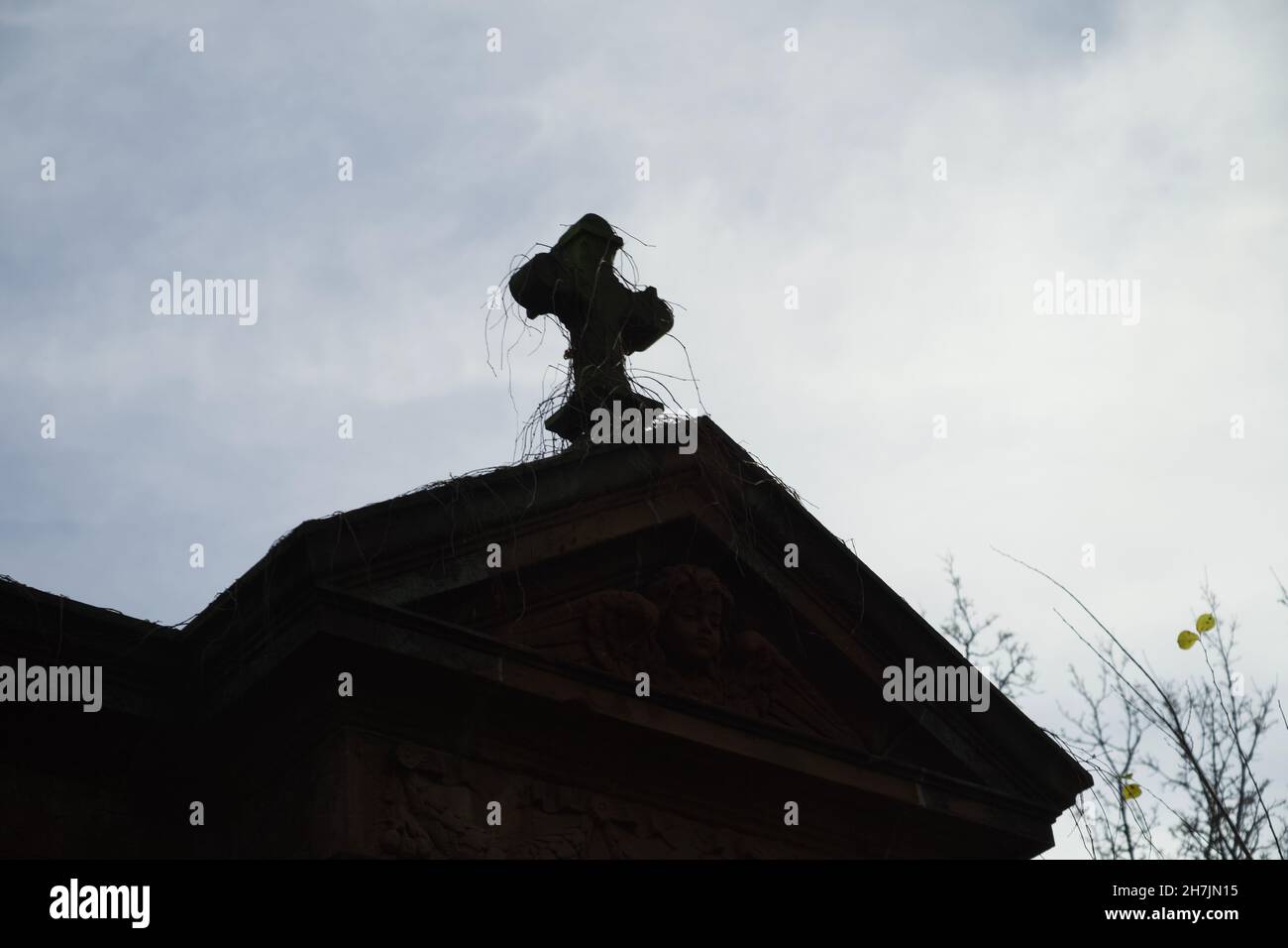 Stone Cross su un'antica tomba che si staglia contro un cielo drammatico in autunno inverno. Girato sul cimitero Alter Luisenstadt Kirchhof a Berlino a B. Foto Stock