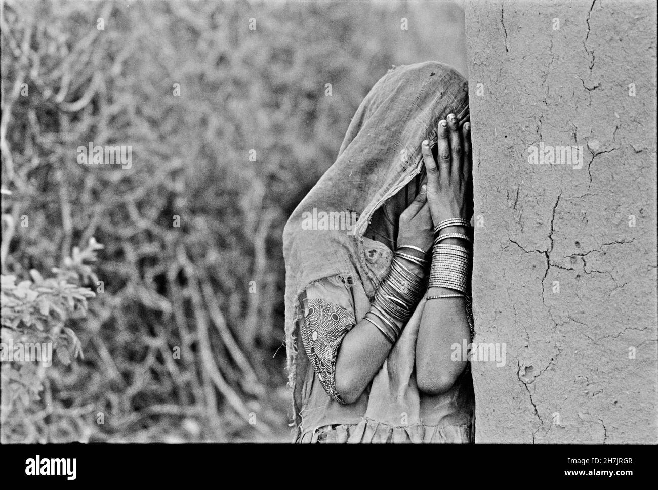 Una bambina pakistana si trova accanto alla loro casa di fango, coprendo il viso con un velo, in un villaggio vicino a Mithi, nella regione desertica di Thar Parkar Foto Stock
