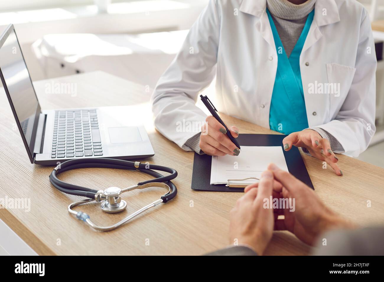 Medico seduto al suo tavolo, parlando con il paziente e scrivere la prescrizione Foto Stock