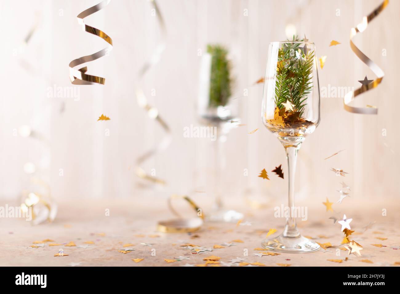 Bicchiere di champagne di Capodanno con scintille all'interno e un albero di abete rosso. Su sfondo bianco di tinsel e nastri. Vista frontale. Foto Stock