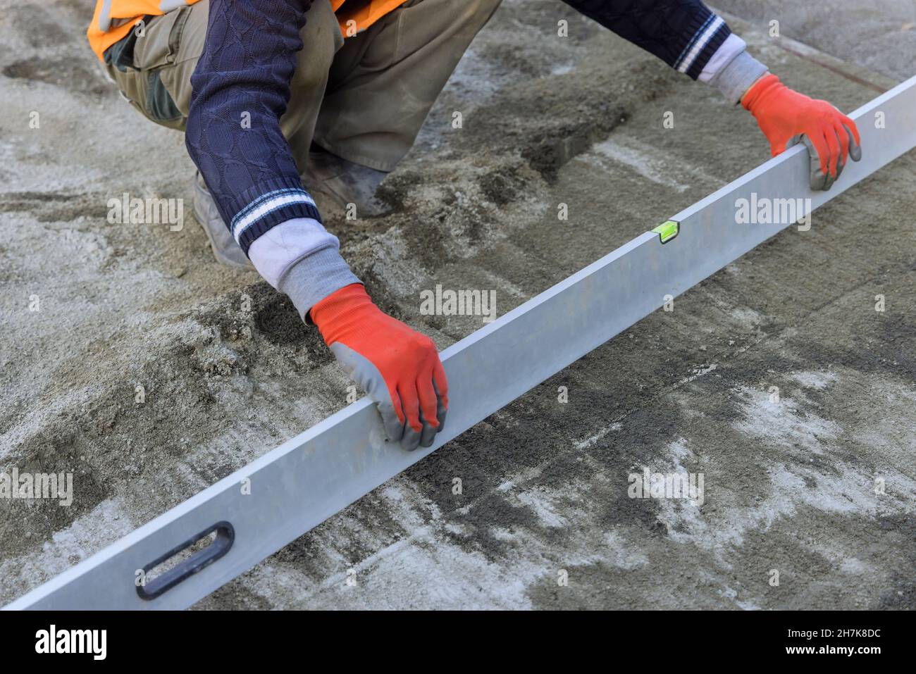 Vista ravvicinata di un operatore che tiene un utensile piano nella preparazione del livellamento su una base sabbiosa delle pietre di pavimentazione Foto Stock