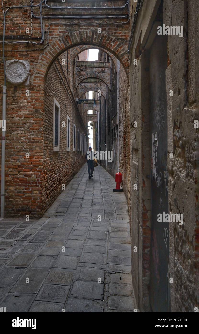 Una tipica stradina ad arco nella città di Venezia, un uomo che cammina Foto Stock