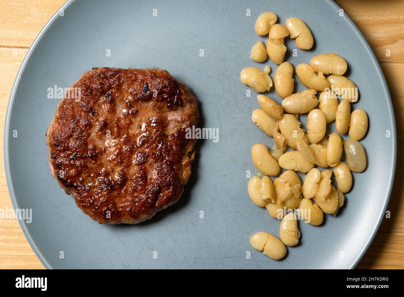 Gustoso hamburger alla griglia servito con fagioli vegetariani cotti in un piatto su un rustico tavolo di legno. Disposizione piatta, vista dall'alto Foto Stock