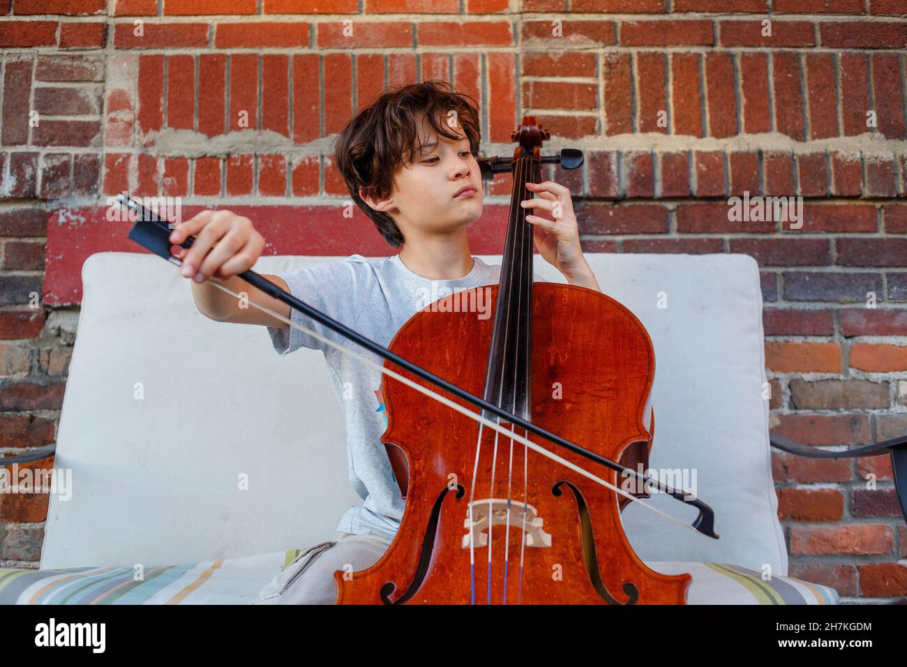 Un ragazzo serio suona il violoncello fuori contro il muro di mattoni Foto Stock
