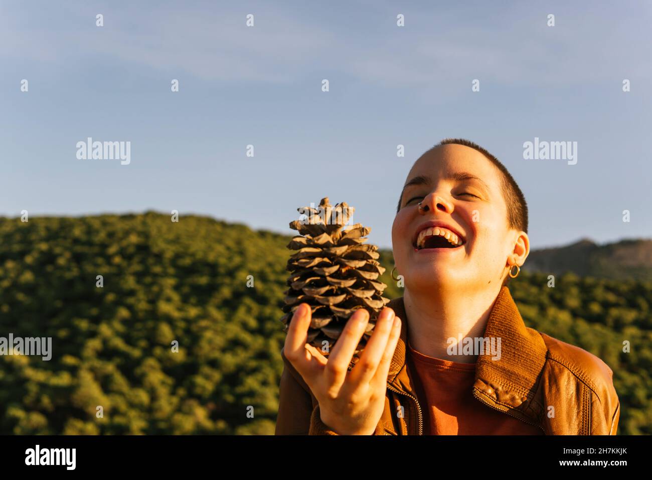 Donna felice tenendo cono di pino durante la giornata di sole Foto Stock