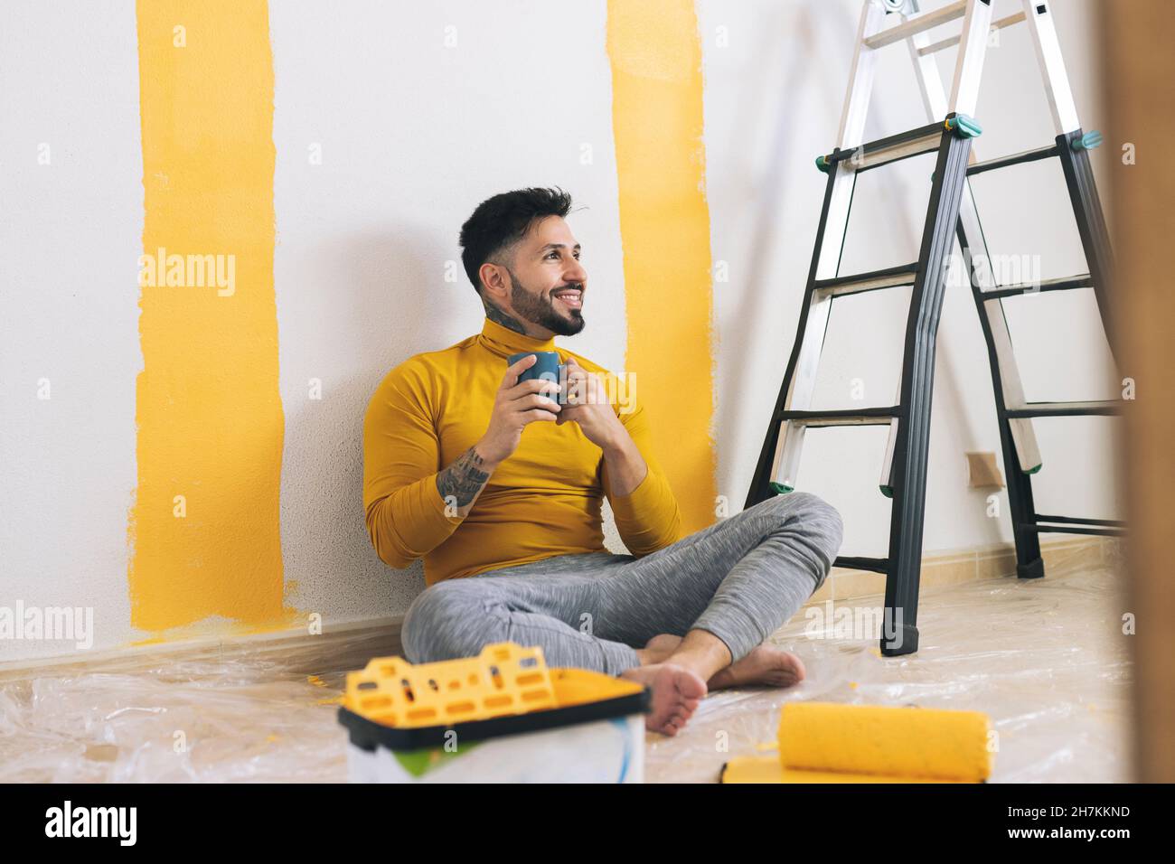 Uomo sorridente con pittura rullo parete in salotto Foto Stock