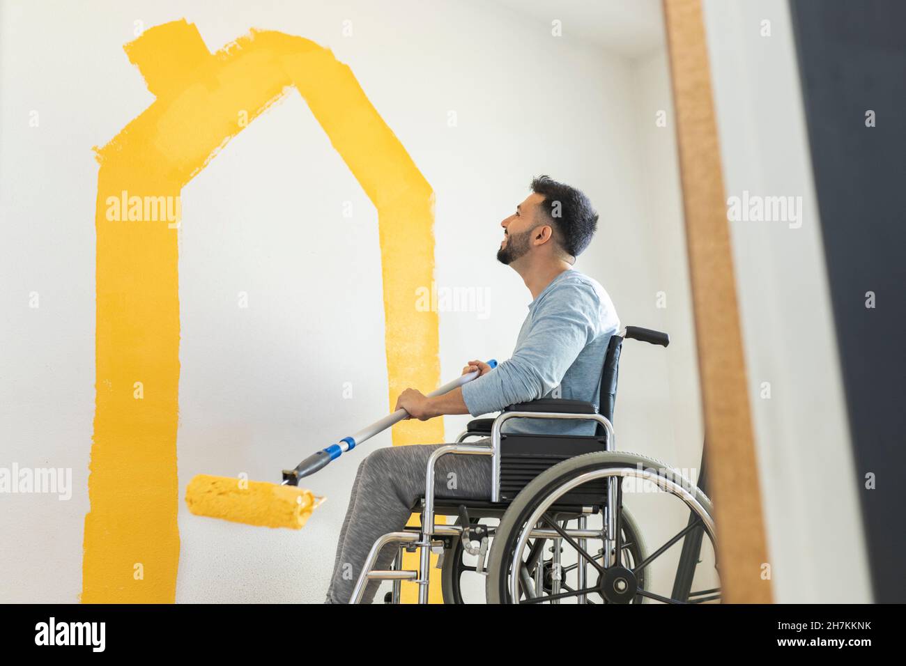 Uomo con disabilità pittura muro attraverso rullo di vernice a casa Foto Stock