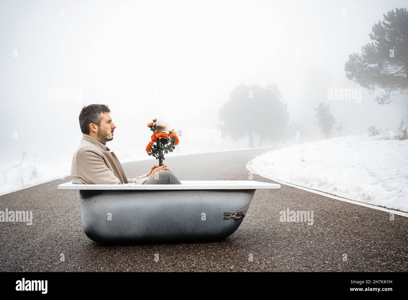 Uomo maturo seduto con fiori in vasca da bagno su strada Foto Stock