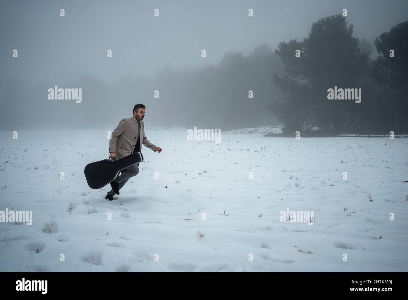Uomo maturo con custodia per chitarra in esecuzione sulla neve Foto Stock