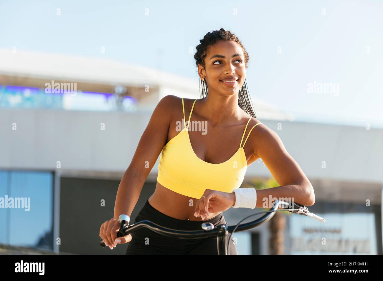Sorridente giovane atleta femminile con bicicletta giorno sognare durante la giornata di sole Foto Stock