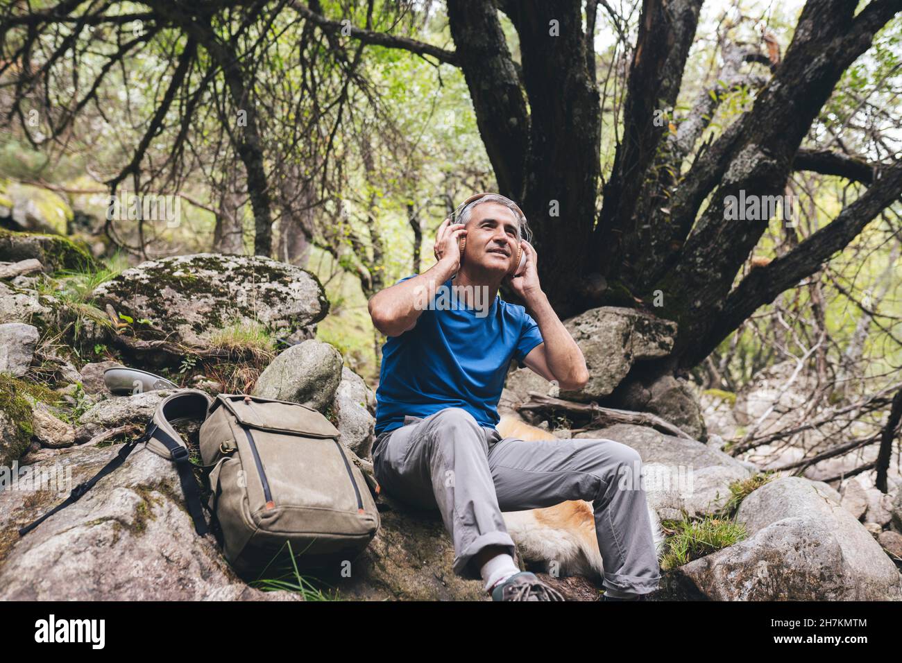 Uomo che registra il suono della natura tramite smartphone mentre si siede da cane nella foresta Foto Stock