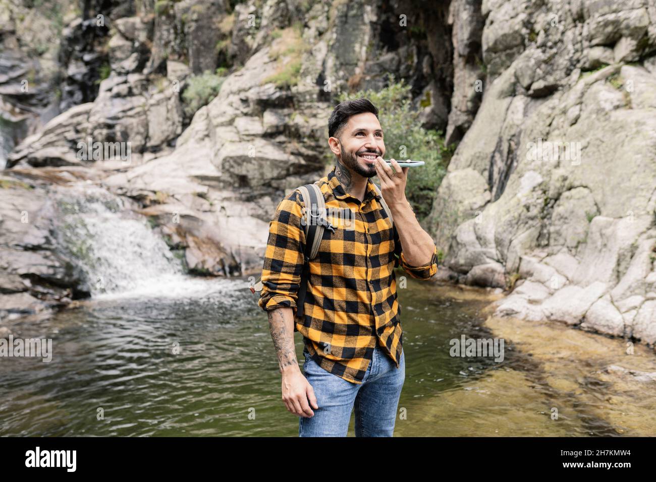 Uomo adulto sorridente che indossa zaino in piedi da stagno nella foresta Foto Stock