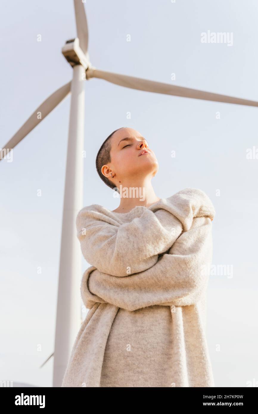 Donna adulta media con occhi chiusi abbracciandosi da turbina eolica Foto Stock