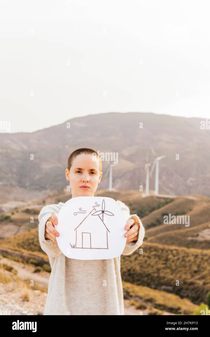 Testa rasata donna che tiene casa disegno sulla montagna Foto Stock