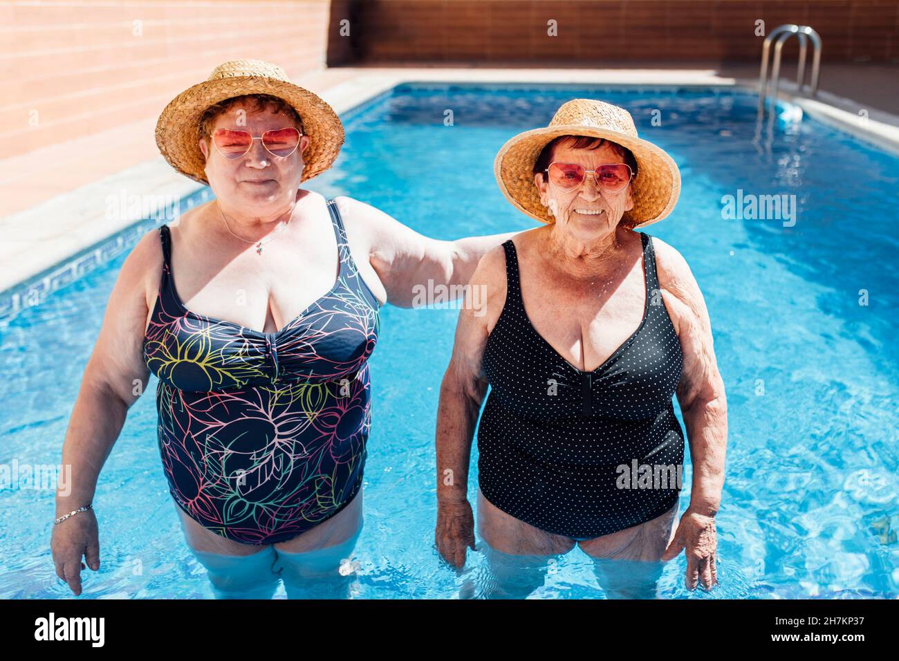 Le amiche indossano un cappello da sole in piscina durante le vacanze Foto Stock