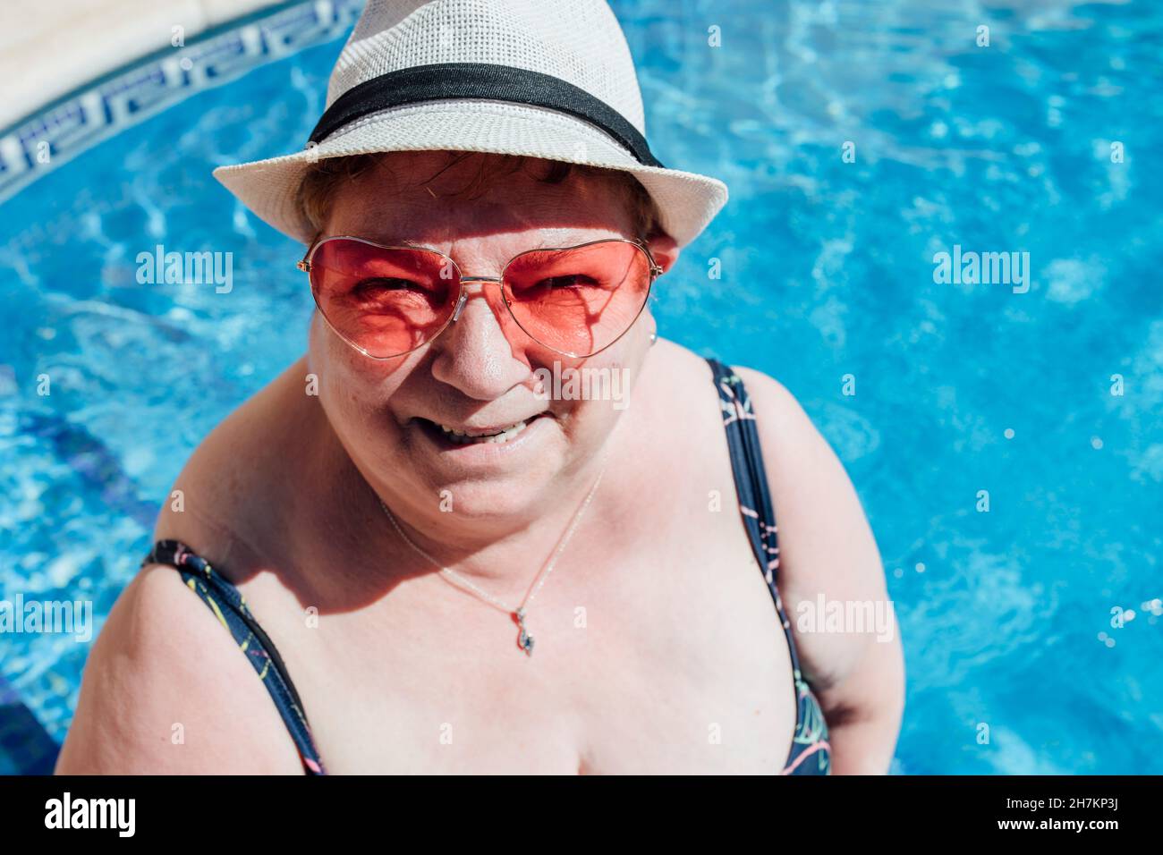 Donna anziana felice che indossa occhiali da sole in piscina Foto Stock