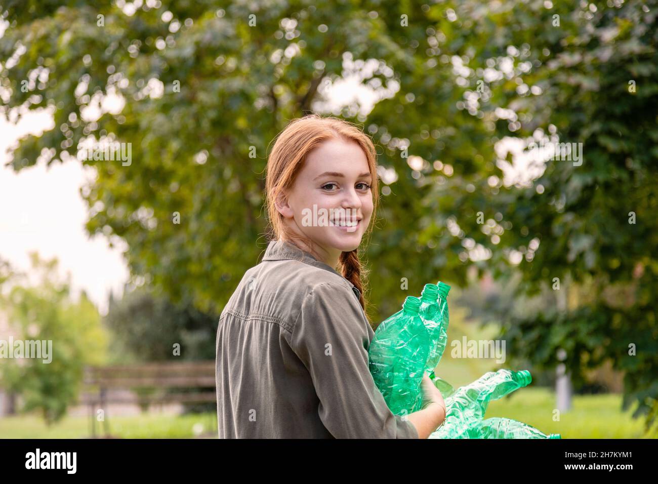 Ambientalista femminile sorridente con bottiglie di plastica che si affacciano sulla spalla in giardino Foto Stock
