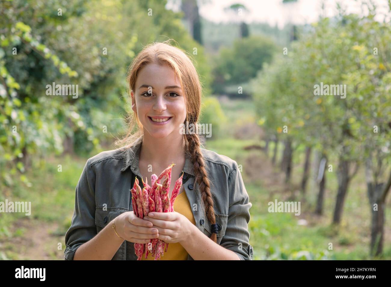 Sorridente bella donna contadina che tiene fagioli freschi in giardino Foto Stock