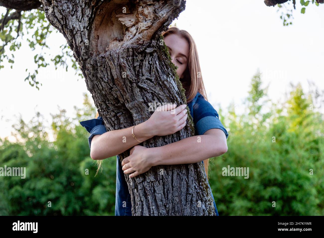 Giovane donna con occhi chiusi abbracciando l'albero Foto Stock