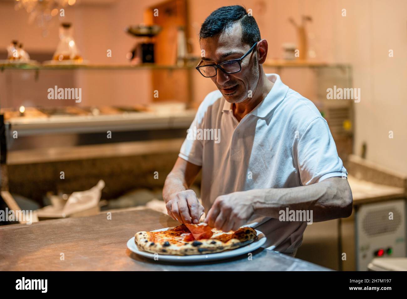 Lo chef aggiunge i condimenti sulla pizza in cucina Foto Stock