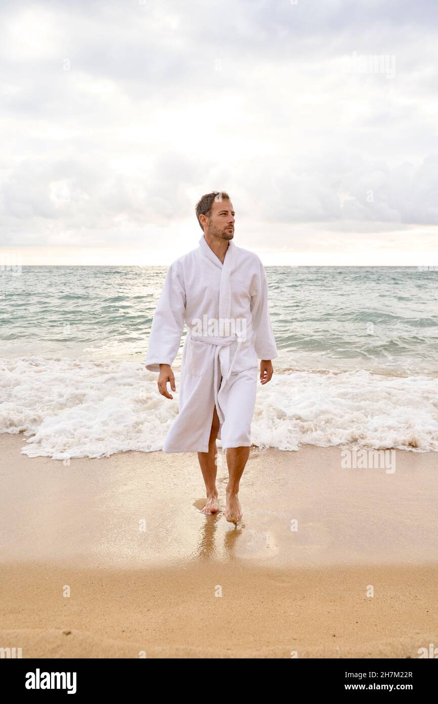 Uomo che indossa l'accappatoio che cammina in spiaggia Foto Stock