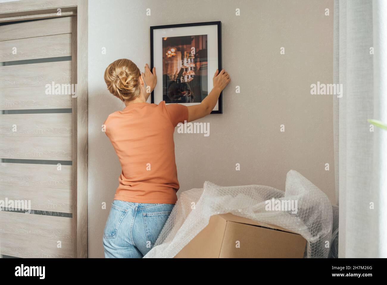 Donna montaggio cornice a parete in appartamento nuovo Foto Stock