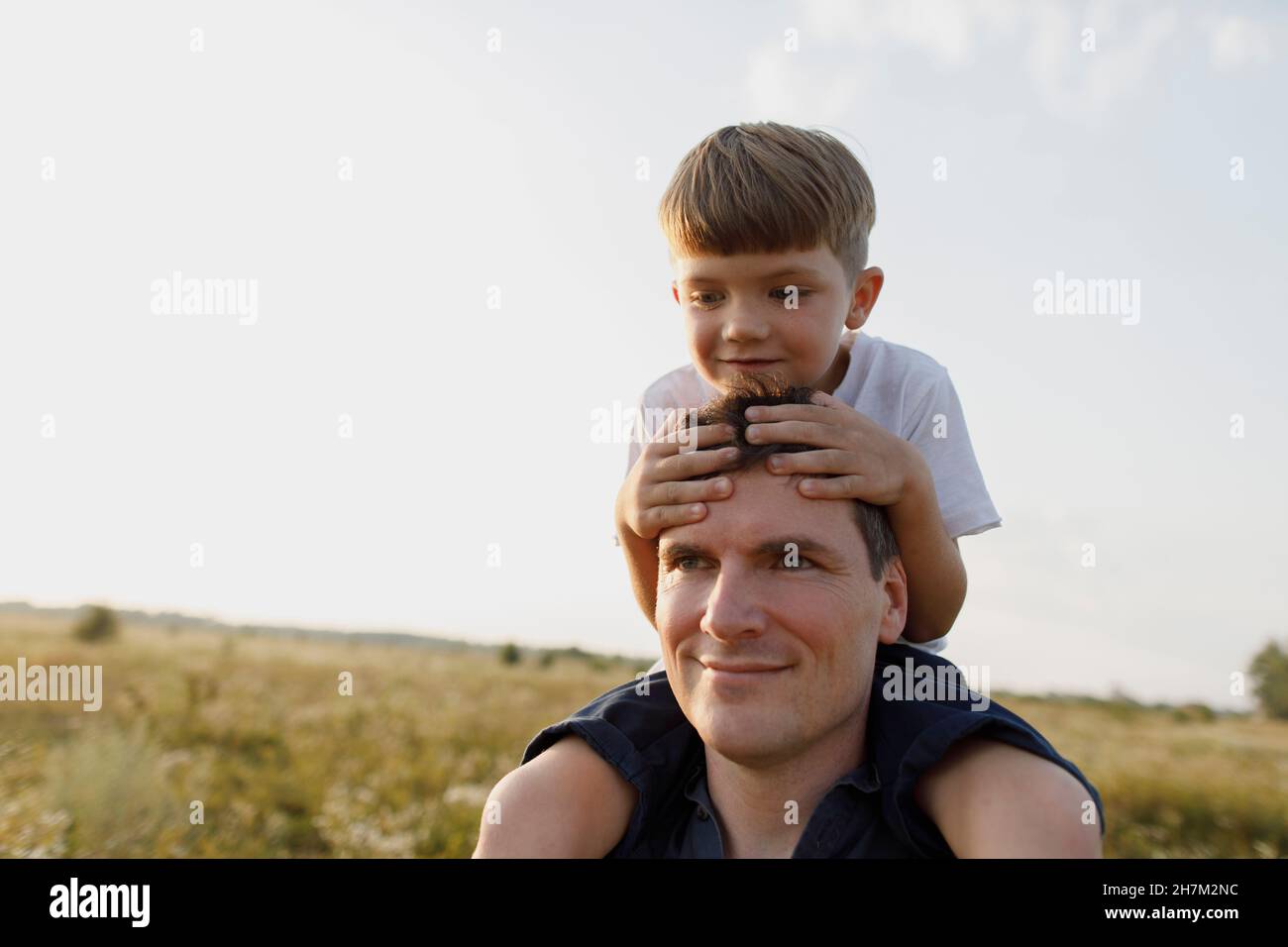 Sorridente padre che porta il figlio sulle spalle al prato Foto Stock