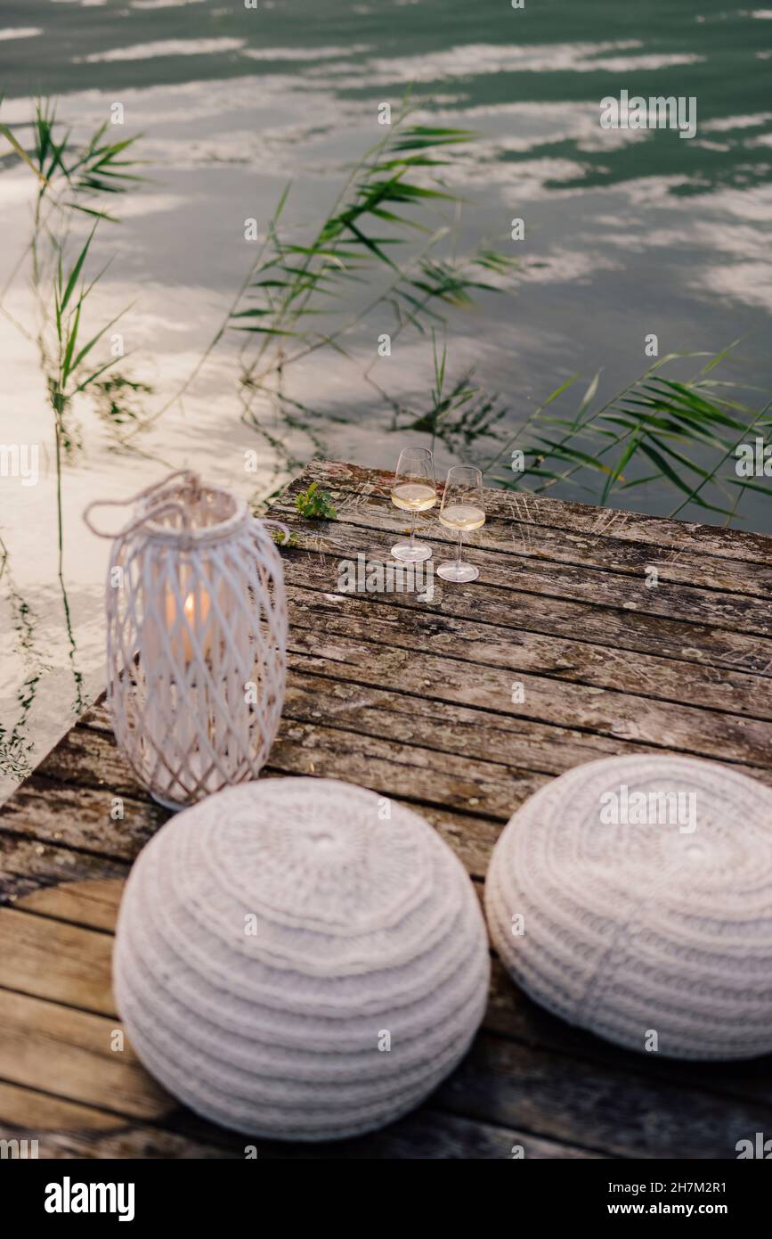 Sacchi di fagioli, lanterna e due bicchieri di vino bianco in piedi sul molo da bordo di lakeshore al crepuscolo Foto Stock