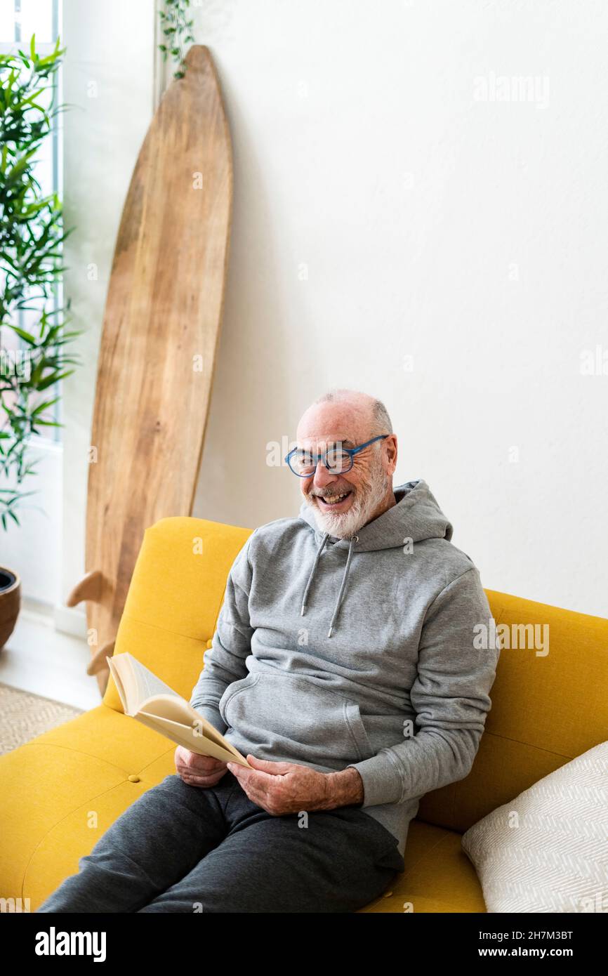 Uomo anziano che legge libro in soggiorno Foto Stock