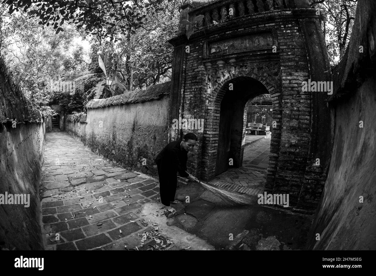 Piccolo vicolo sul piccolo vicolo per il tempio, una donna si aggroviglia le foglie cadute, una bella scena tranquilla e pacifica. Foto Stock