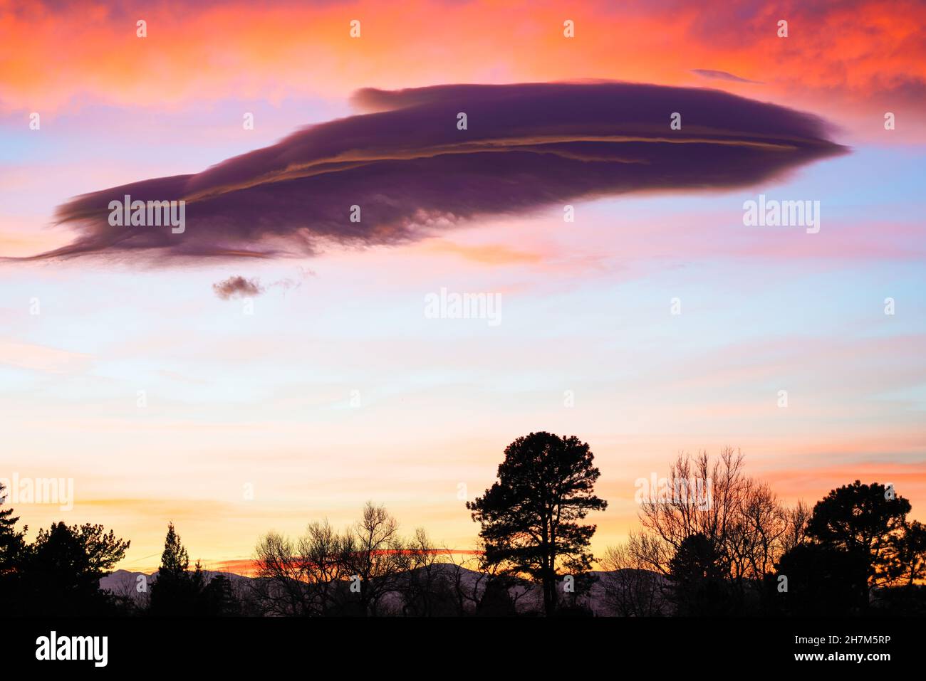 Una nube sottile e piume aggiunge un interesse stravagante a questo colorato tramonto del Colorado. Foto Stock