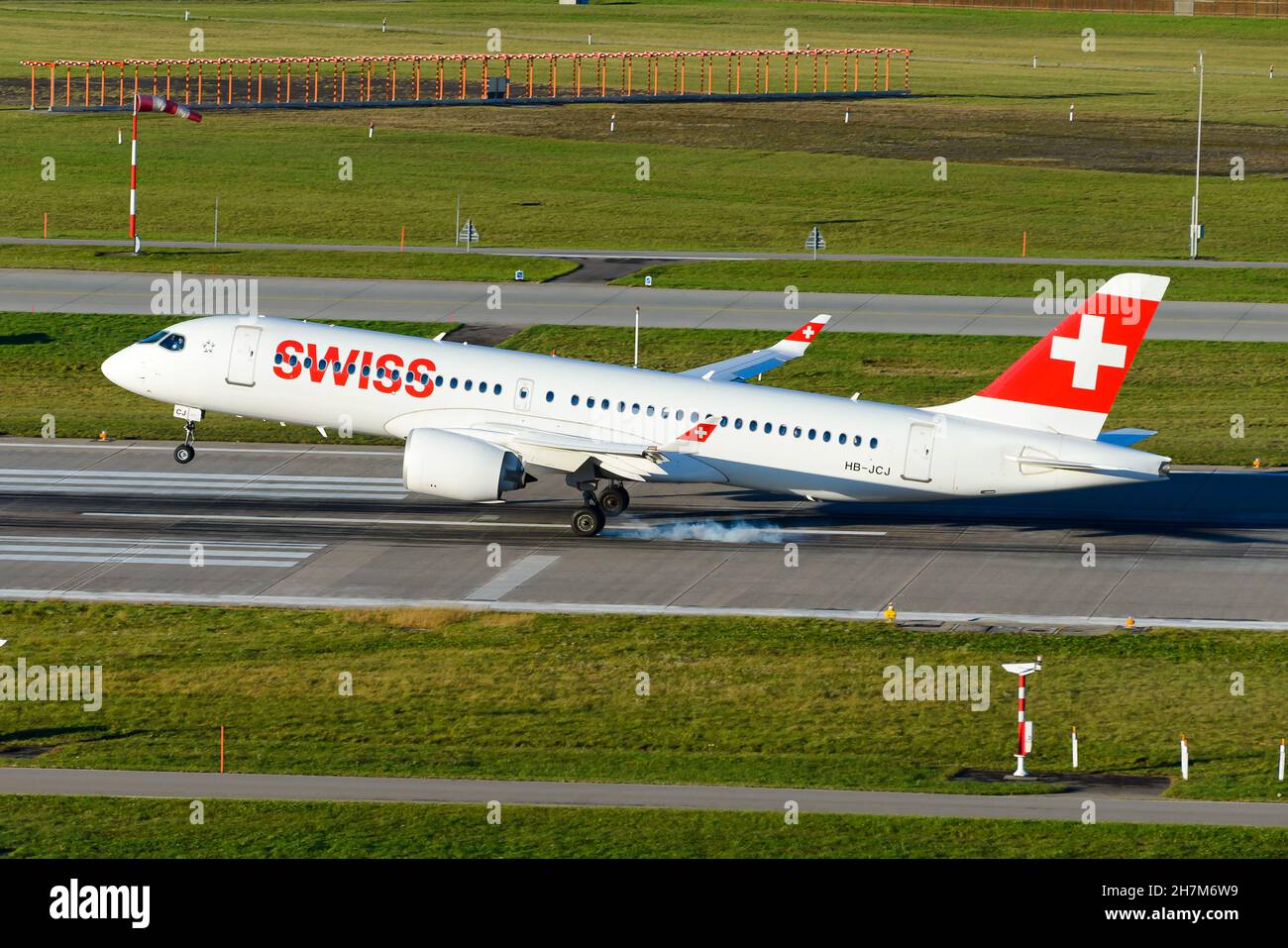 Atterraggio dell'aeromobile Airbus A220 di Swiss Airlines. Nuovo moderno velivolo Bombardier CS300 di Swiss Air Lines che fuma il carrello principale. Foto Stock