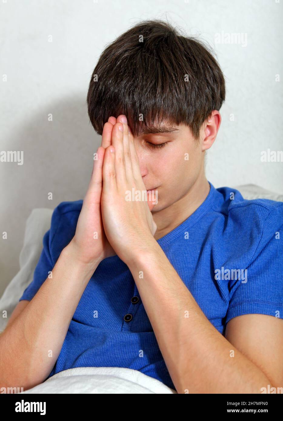 Giovane uomo che prega sul letto a casa Foto Stock