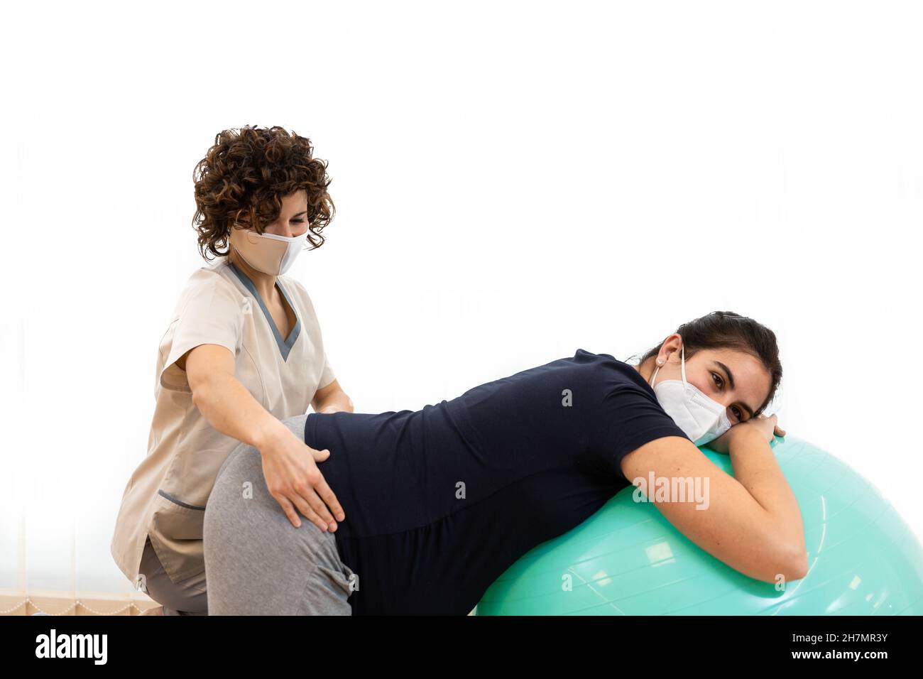 Una donna incinta che fa pilates gli esercizi con una sfera con l'aiuto del suo fisioterapista Foto Stock