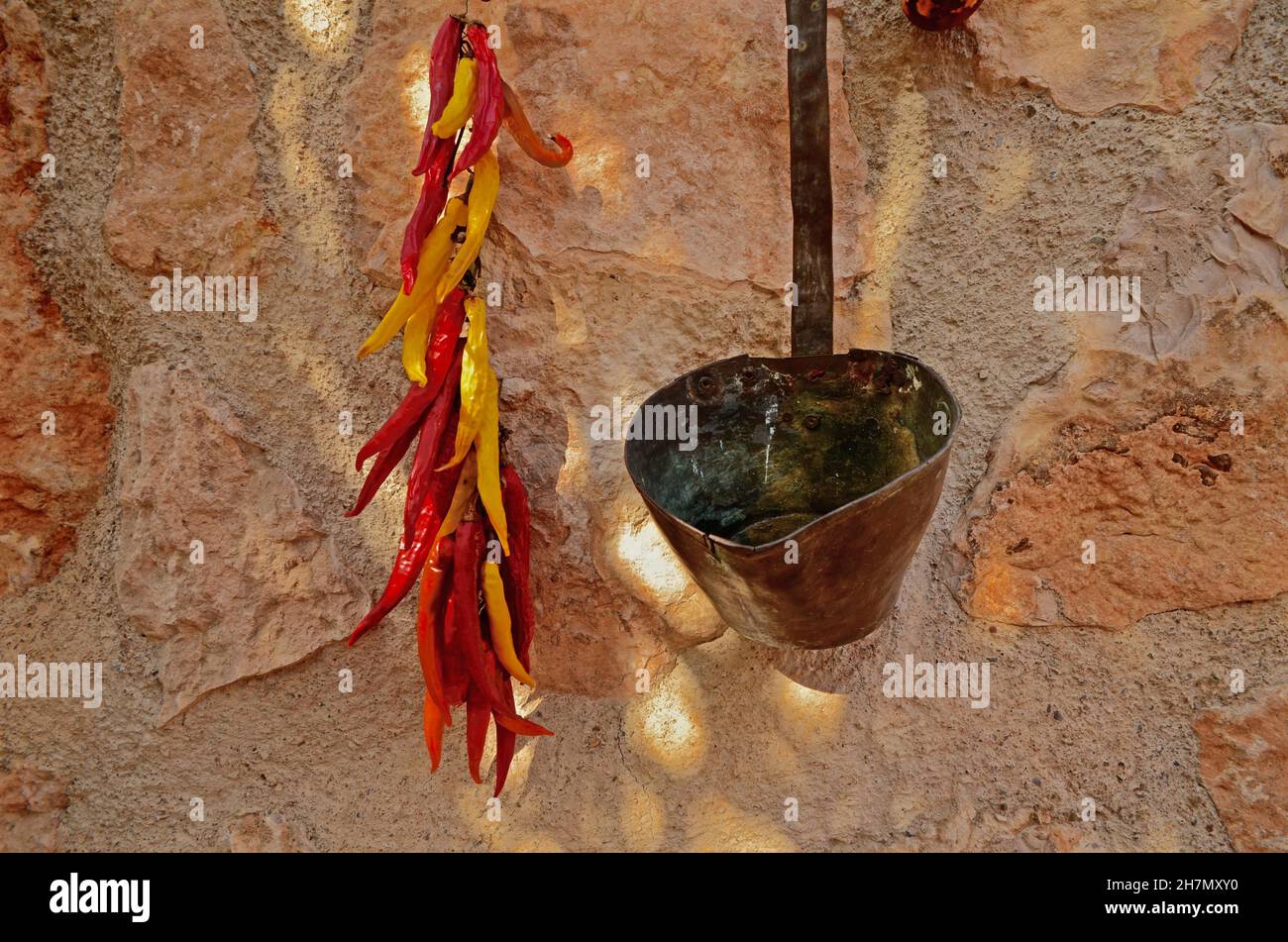Peperoni rossi e gialli secchi su una parete della casa, mestolo di rame, vita di campagna spagnola, Andalusia, Spagna Foto Stock