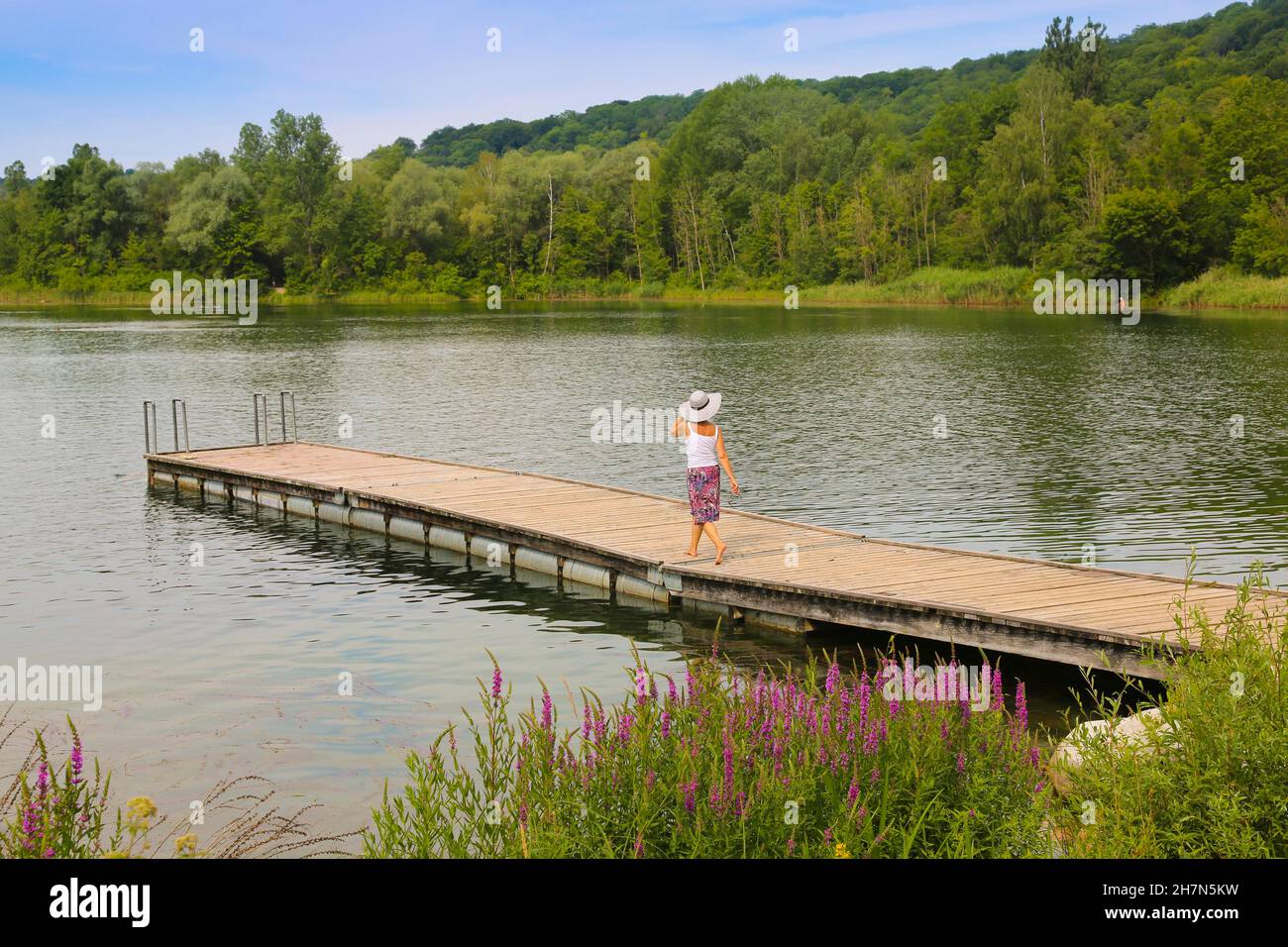 Donna in cappello e gonna a piedi sul molo, Pfuhler See, acque di balneazione, Neu-Ulm, Baviera, Germania Foto Stock